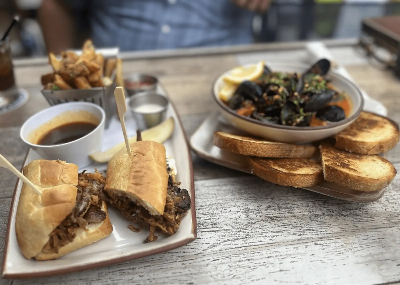 A sandwich served with mussels and grilled bread on an outdoor table