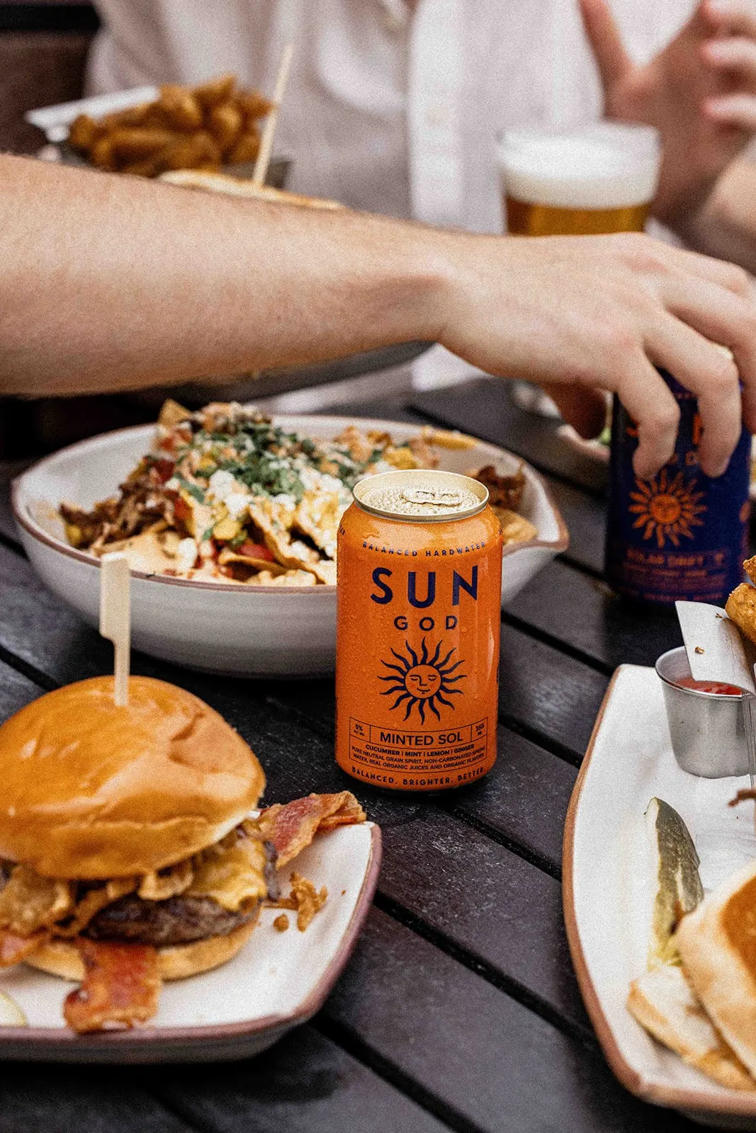 A can of SUNGOD Minted Sol on a picnic table beside a burger and a loaded bowl