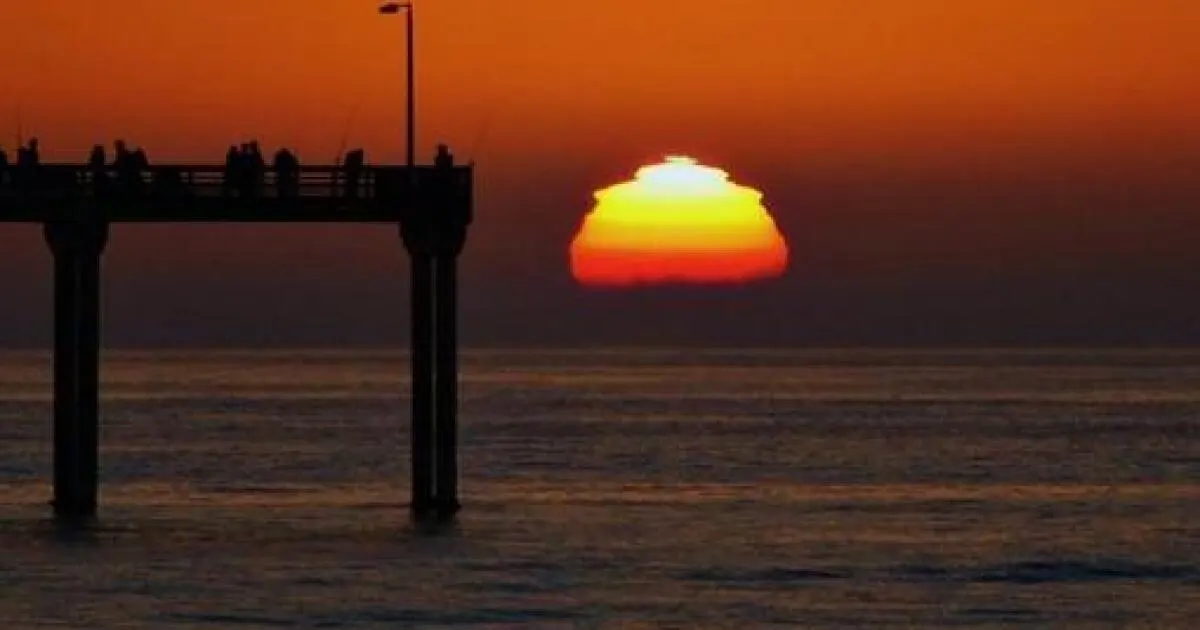 The sun setting into the ocean beside a silhouetted San Diego pier