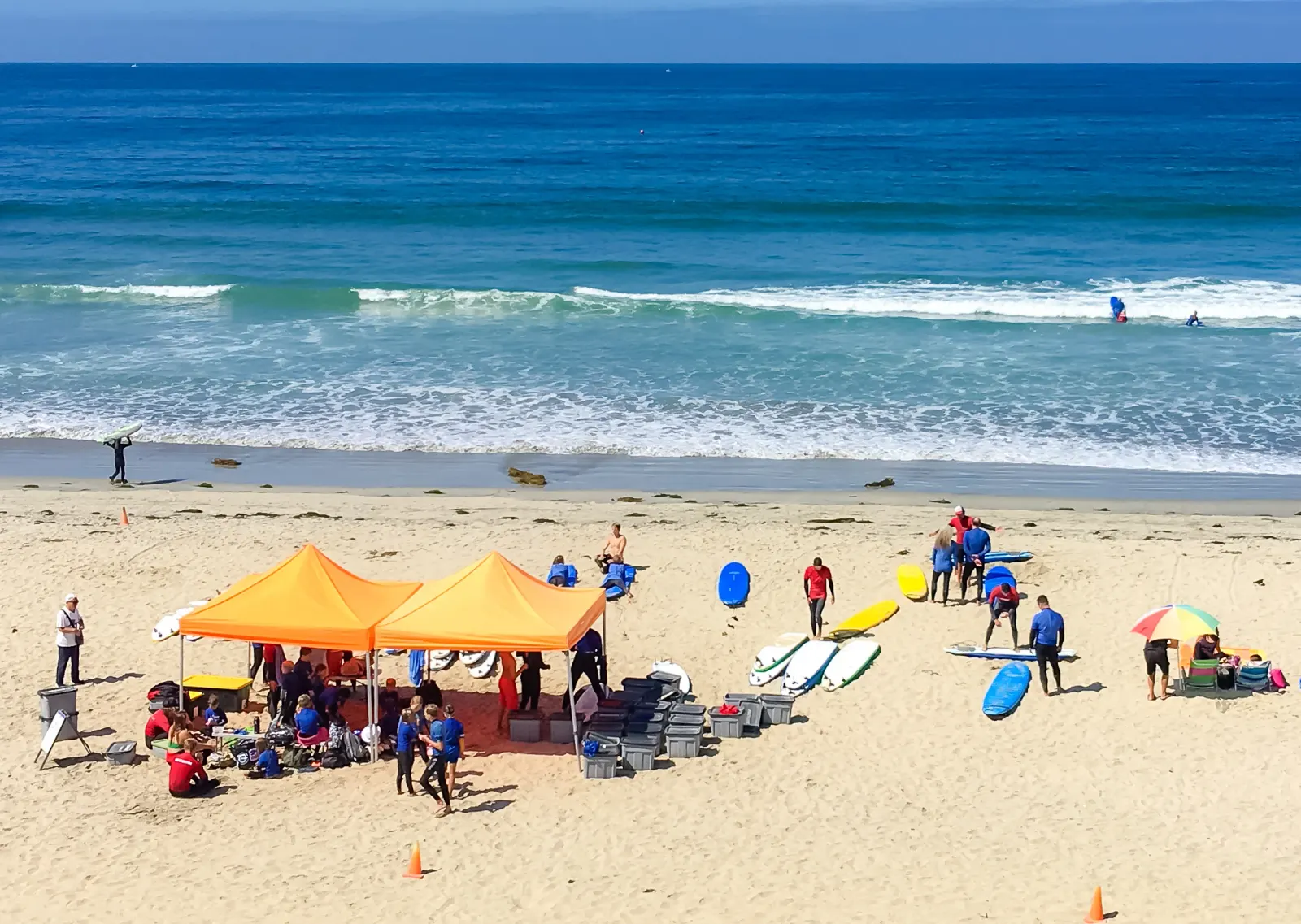 Canopies and surfboards set up on the sand as waves break behind