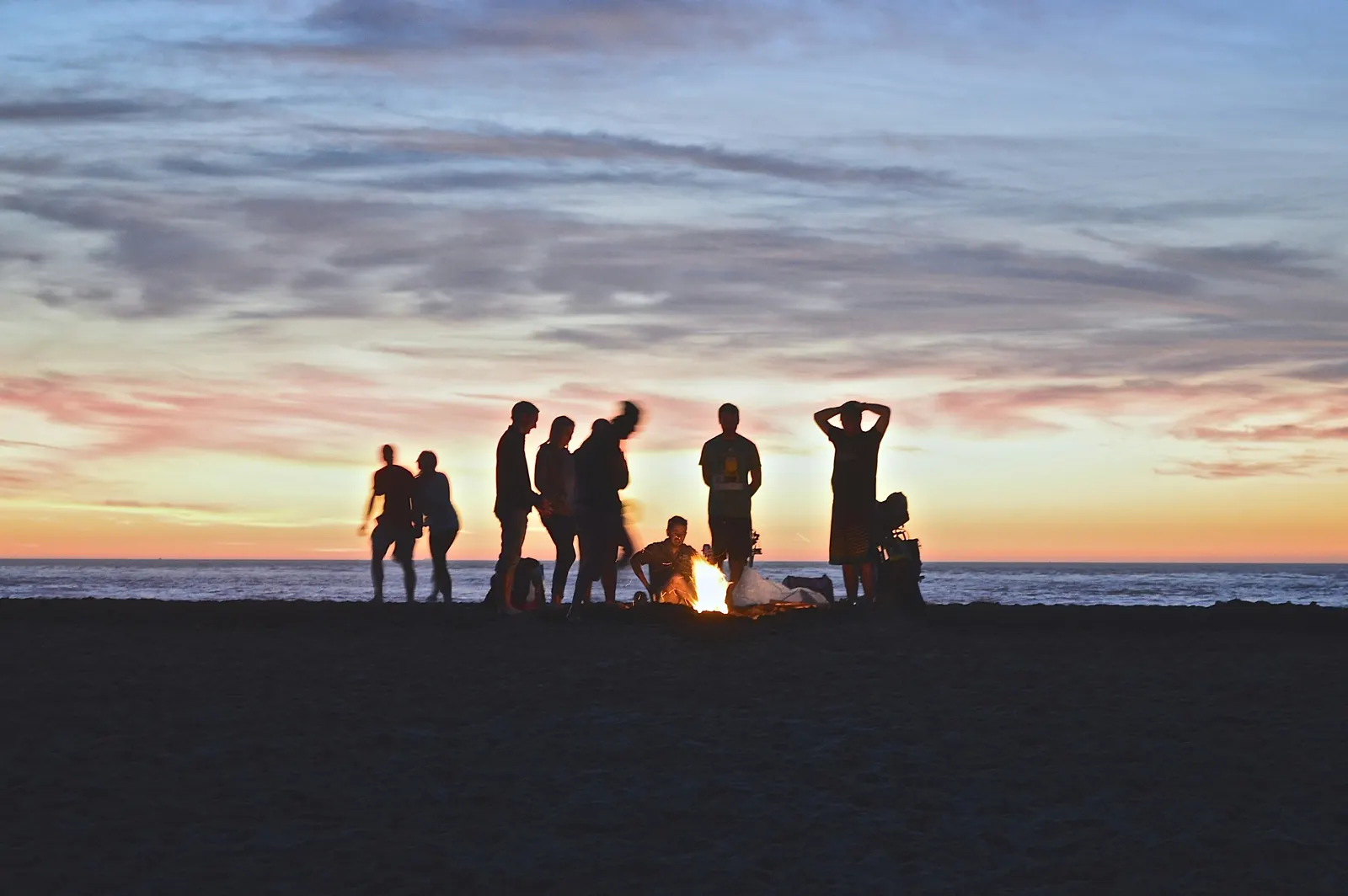A group gathered around a beach bonfire at dusk