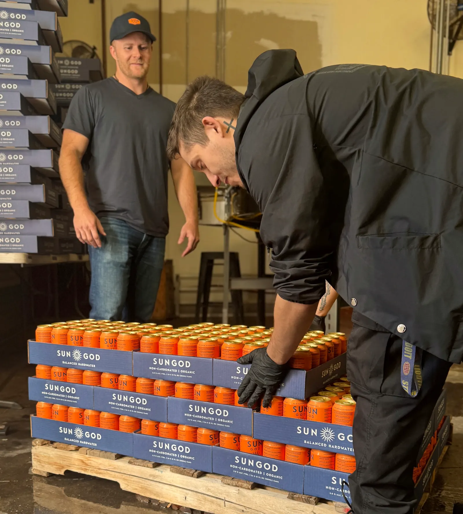 Two of the founders hand-stacking cases of SUNGOD onto a pallet